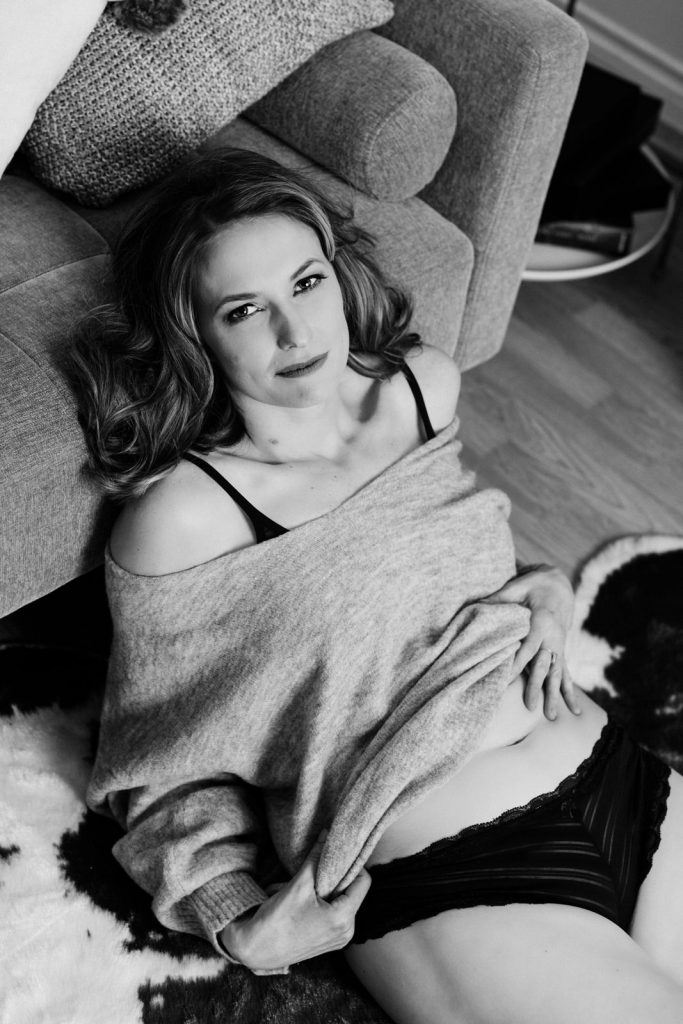 Woman on floor leaning against couch touching her bare stomach in boudoir photo