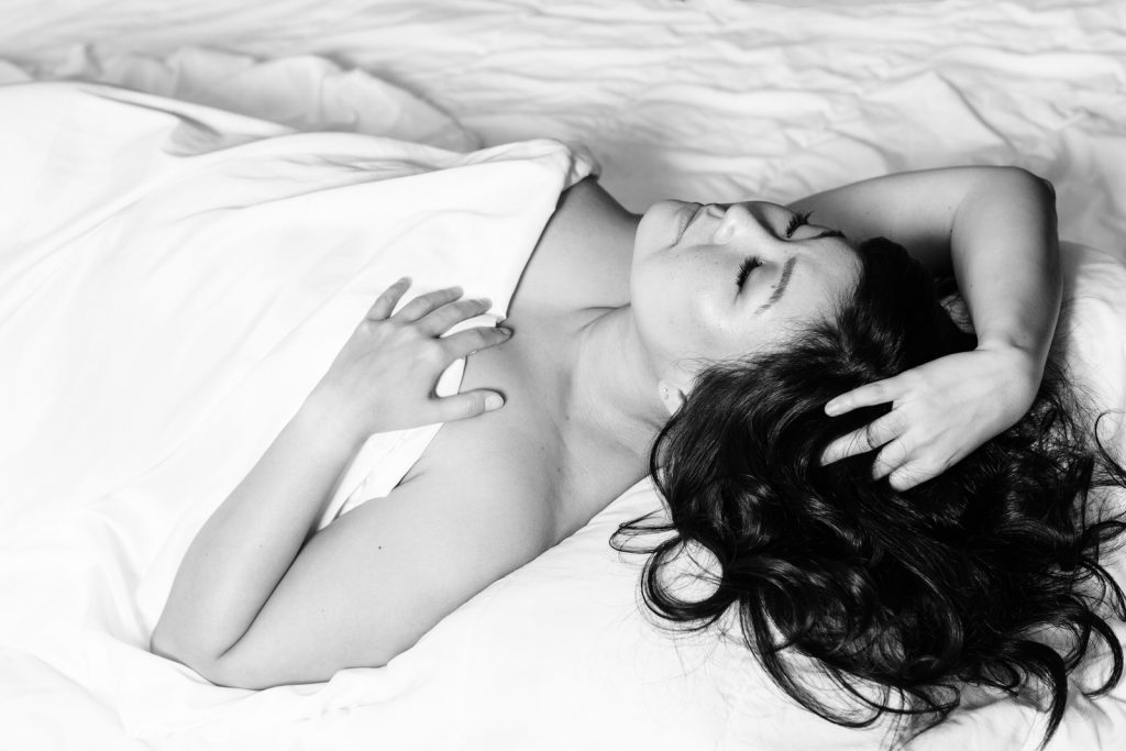 Woman laying on her back covered by white sheet in boudoir photo