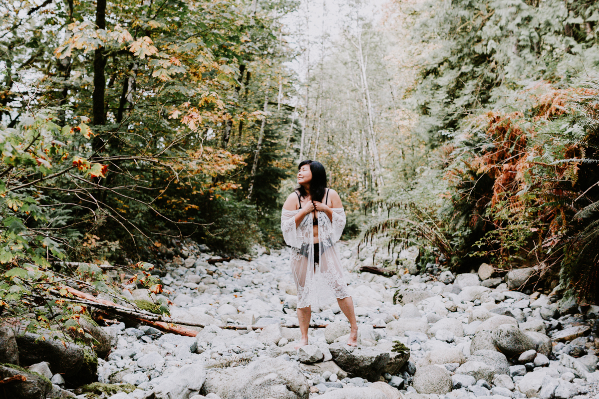 Woman in lace outfit standing on rocks surrounded by trees doing boudoir photos