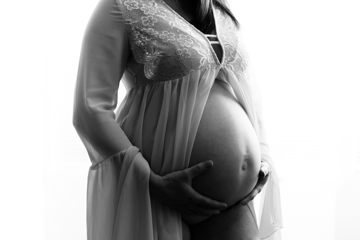 Maternity Boudoir Photos of pregnant woman in white lace gown showing bare belly