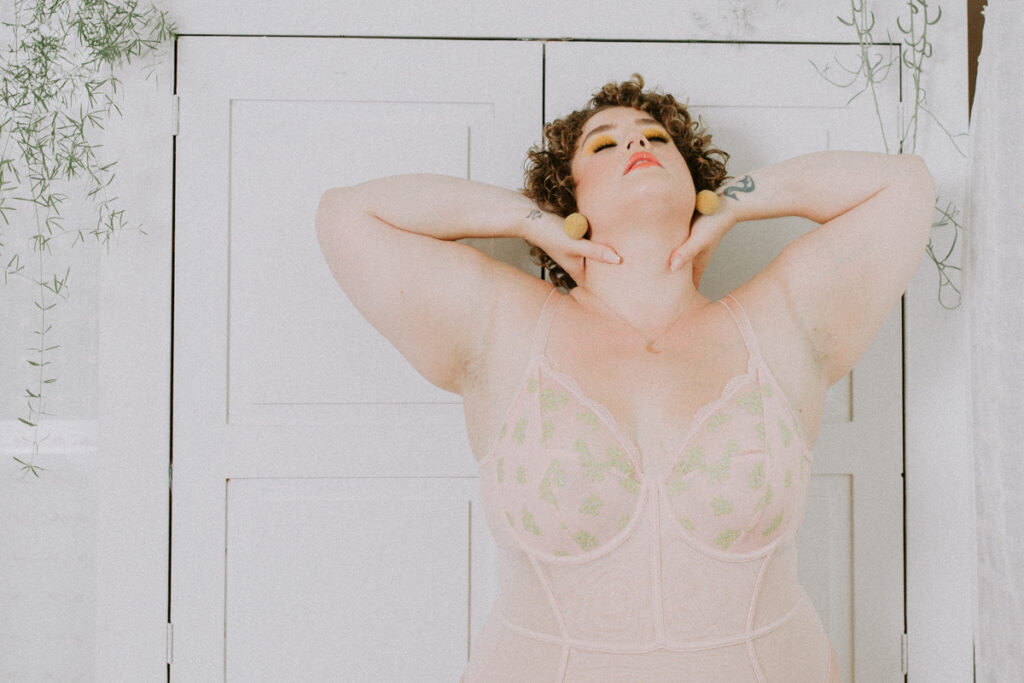 Boudoir image of beautiful and fat woman wearing lingerie and standing tall holding hands to he neck