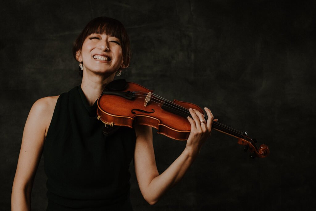 Cathy 40 over 40. A woman laughing with eyes closed and holding a violin