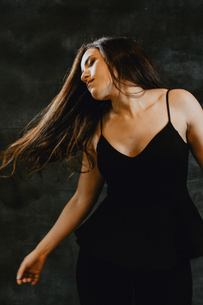 A woman dancing wearing a black strappy dress her hair swinging to the side, shot by a Vancouver Portrait Photographer