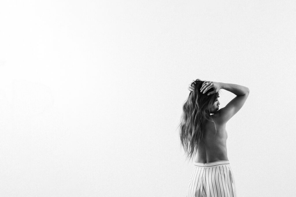 white-backdrop-vancouver-intimate-portraits of woman standing wearing pants and no top showing bare back with long hair falling over back