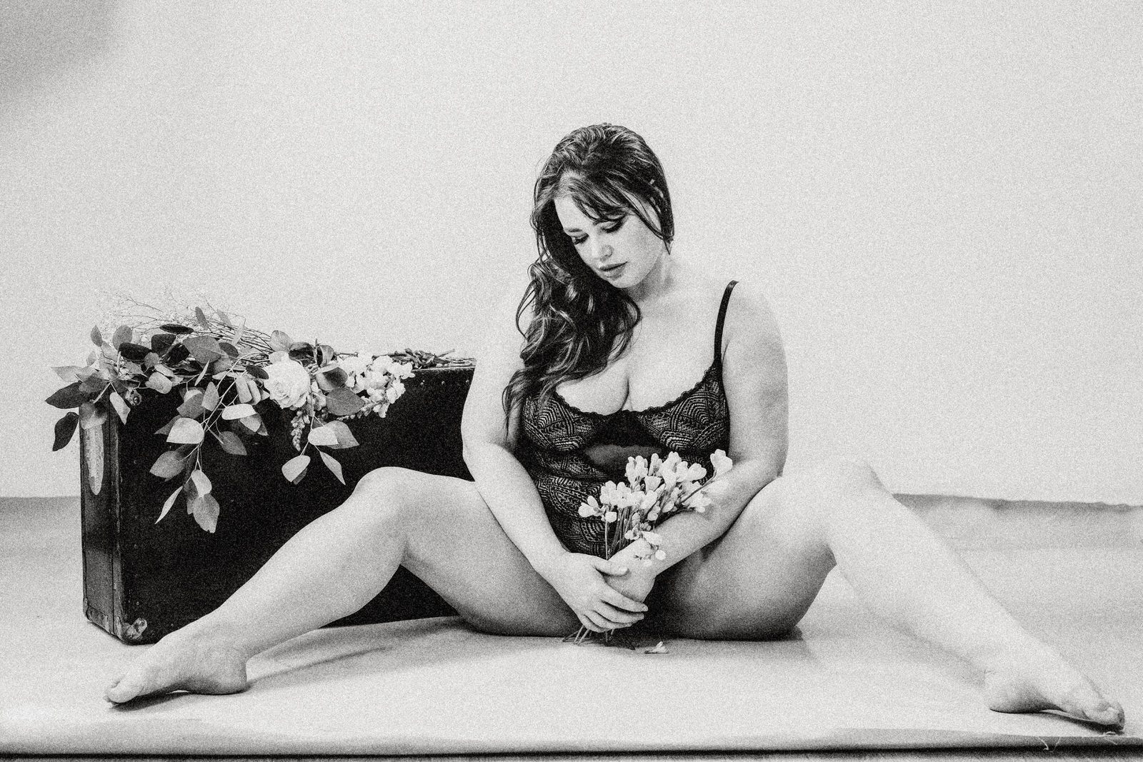 Plus size boudoir photo of a woman sitting on the floor with legs apart holding flowers