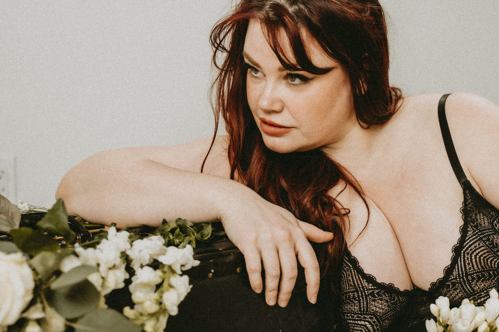 Plus size boudoir photo of a woman leaning holding flowers