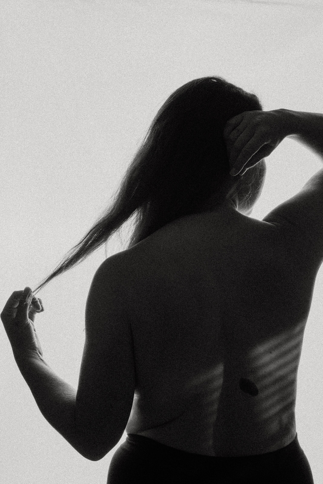 fine art nude image of woman's back and hands holding hair