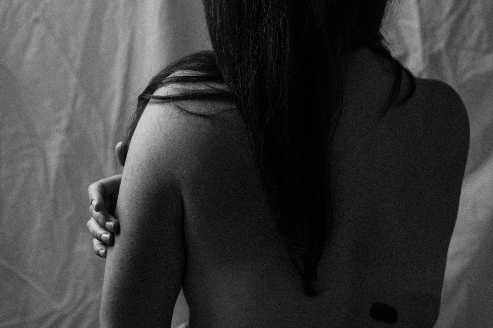 fine art nude image of woman's back, hair falling down back and hand on her arm