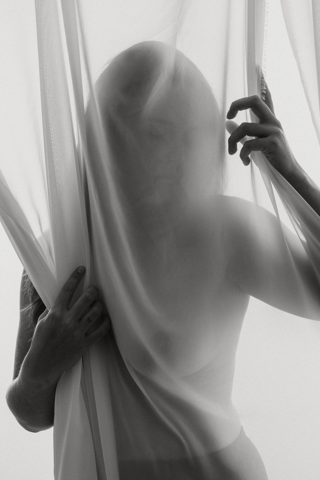 fine art nude photo of a woman behind a sheer curtain and holding edges of curtain