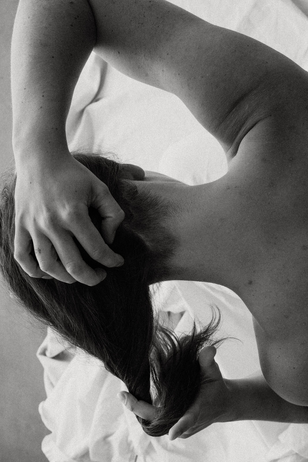 black and white boudoir image of back of woman's neck with hands holding hair off her back