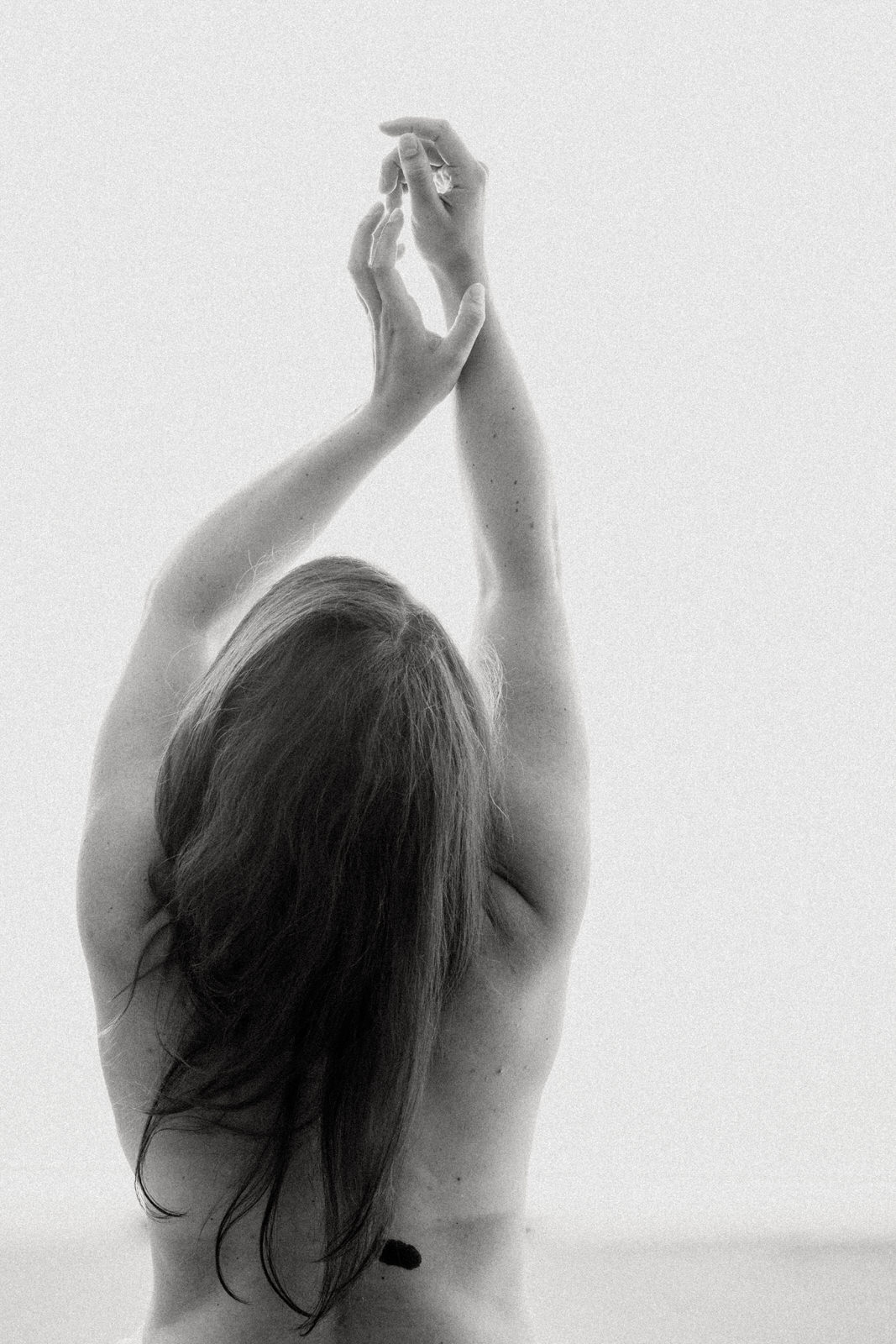 black and white fine art nude photo of a woman reaching up above head with hair falling down her back