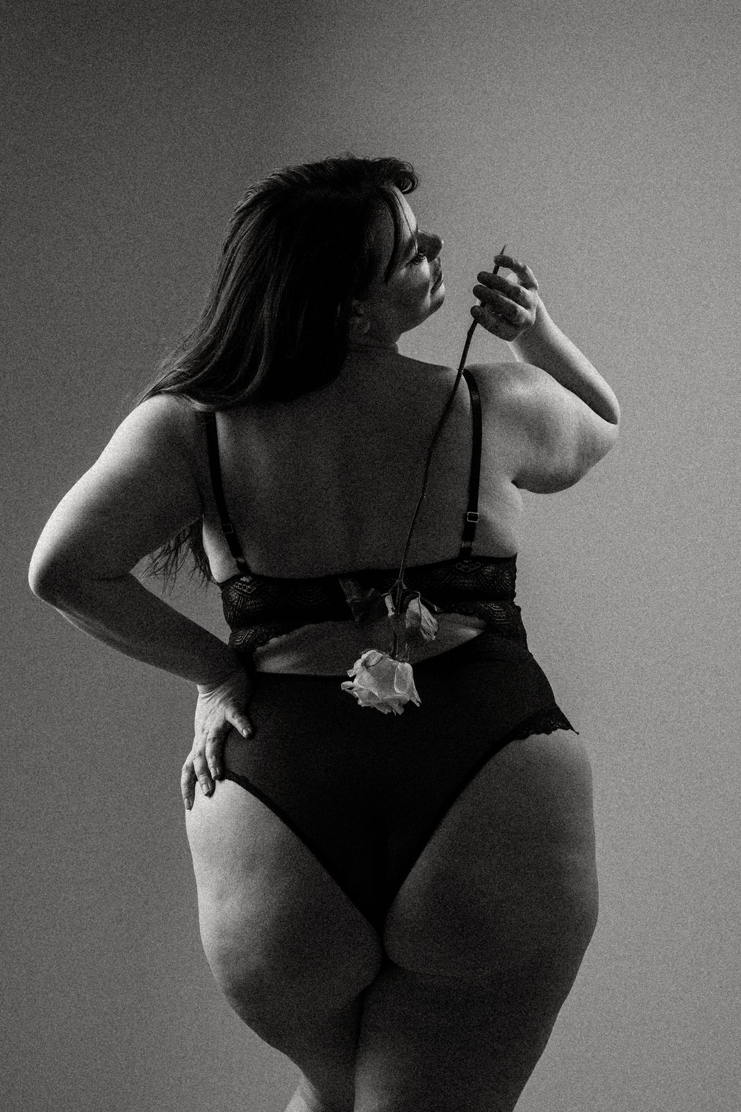 Plus size boudoir photo of a woman's back holding a rose over her shoulder hanging down her back