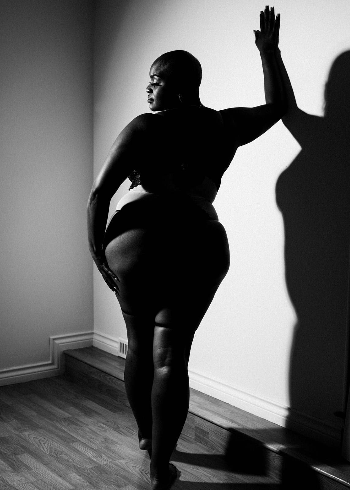 vancouver boudoir photographer image of plus size black woman with alopecia standing with arm against wall